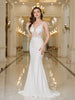Woman in a white evening gown standing in an elegant hallway with chandeliers.